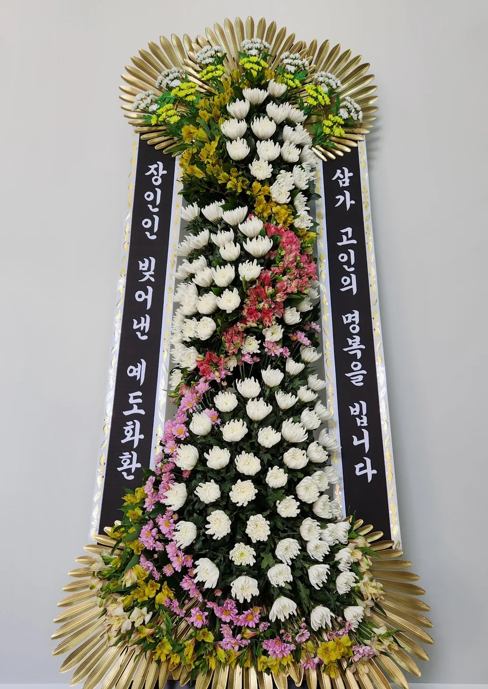 예도 근조화환의 전체 정면 모습. 흰 국화 사이로 분홍색과 노란색 꽃선이 이어진다.
